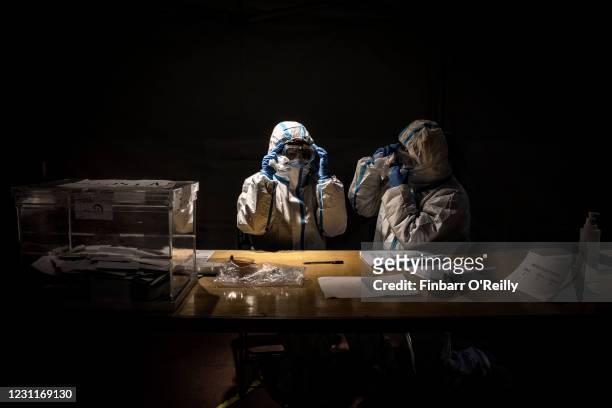 Election workers wearing protective equipment clean their fogged goggles while waiting for voters during the final hour of voting, which was...