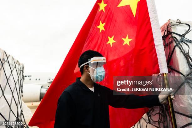Man wearing a face mask holds the Chinese national flag as he looks on while workers offload an Air Zimbabwe aeroplane with a donation of 200,000...