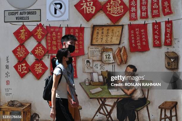 Couple walk past wall murals in a back alley in the Chinatown area of Singapore on February 15, 2021.