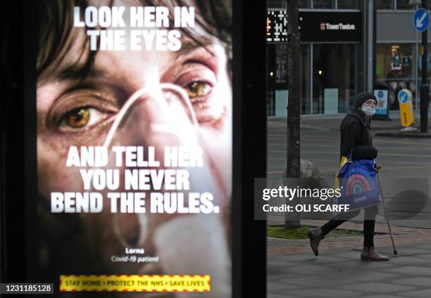 Pedestrian wearing a face covering walks past a Government Covid-19 information poster in Manchester, northern England, on February 15, 2021. -...