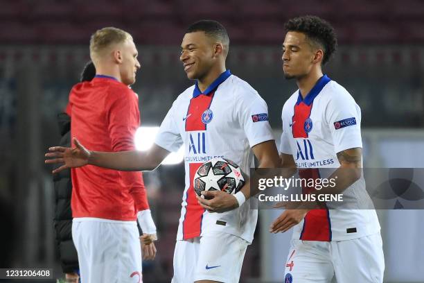 Paris Saint-Germain's French forward Kylian Mbappe walks while holding the match ball for scoring a hat trick next to Paris Saint-Germain's German...