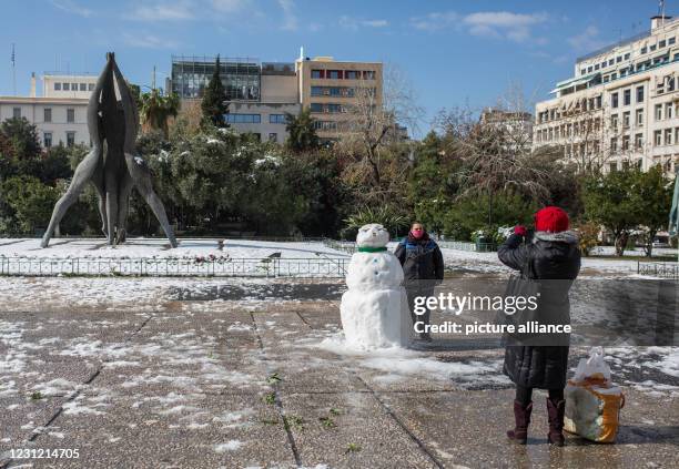 February 2021, Greece, Athen: A woman takes a photo of a man standing next to a snowman in central Athens. A strict lockdown has been in effect for...