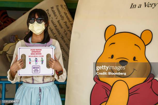 An employee holds a sign reminding visitors to maintain social distance at the Many Adventures of Winnie the Pooh ride at Walt Disney Co.'s...