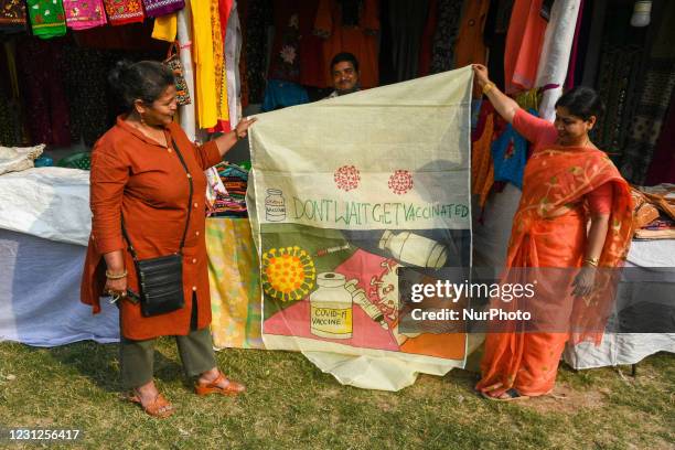 Shop owners displays a saree for sale with COVID vaccination message written on it at the fair ground . Artisan from all parts of Bengal came to...