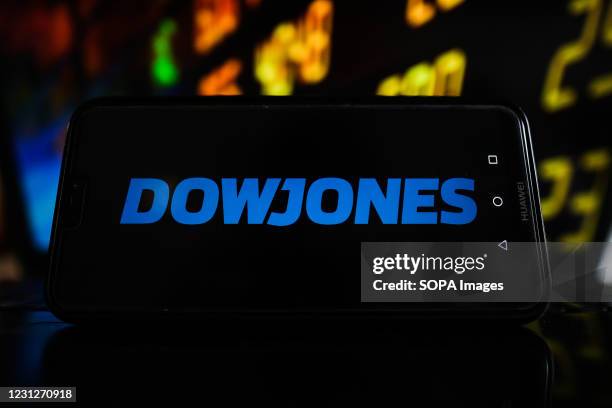 In this photo illustration a Dow Jones logo seen displayed on a smartphone with stock market values in the background.