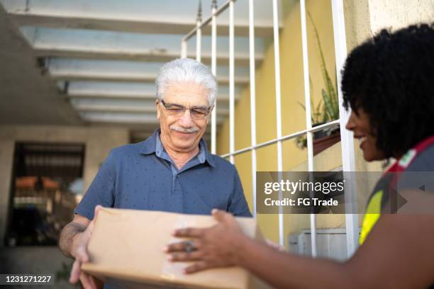 female courier delivering packages to senior man at his front door - post truth stock pictures, royalty-free photos & images