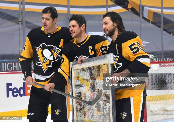 Sidney Crosby of the Pittsburgh Penguins poses for photos with Evgeni Malkin and Kris Letang during pregame ceremonies honoring Crosby's 1000th game...