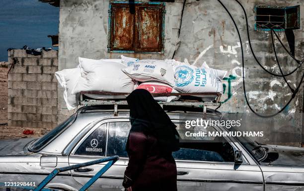 Woman walks past a vehicle loaded on top with sacks of humanitarian aid provided by the United Nations Relief and Works Agency at a distribution...