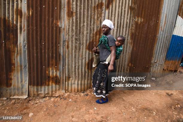 Woman walks along an Old street in Kibera Slums with her little baby on Her back.