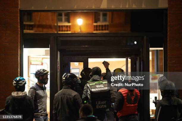 Delivery workers gesture in front of restaurant to obtain their orders to deliver. Food delivery industry has boomed in the past year as the pandemic...