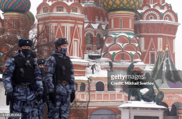 Russian National Guard Service soldiers wearing face mask protecting against the coronavirus look on workers removing snow from the roof of the...