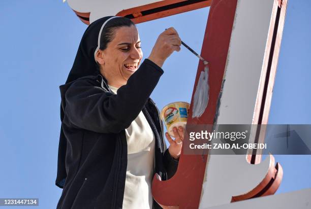 Massir Hayat, a Catholic nun in charge of youth organisation at the Immaculate Mary Dominican Sisters Convent, adds a coat of paint to the crucifix...