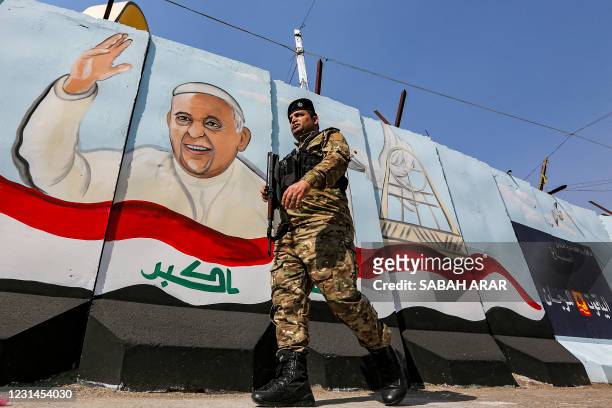 Member of the Iraqi forces walks past a mural depicting Pope Francis waving next to an Iraqi national flag drawn on a blast wall outside the Syriac...