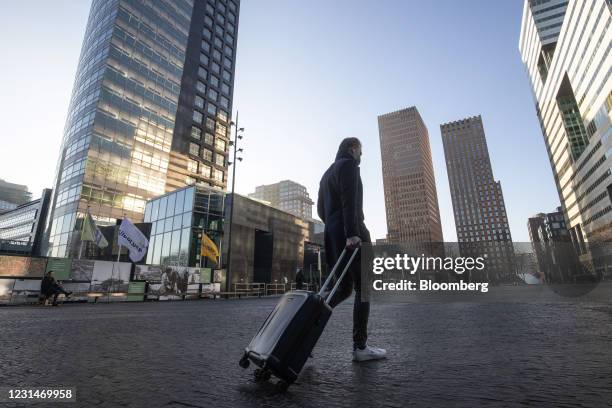 Morning commuter wheels luggage near skyscraper offices in the Zuidas business district in Amsterdam, Netherlands, on Tuesday, March 2, 2021....