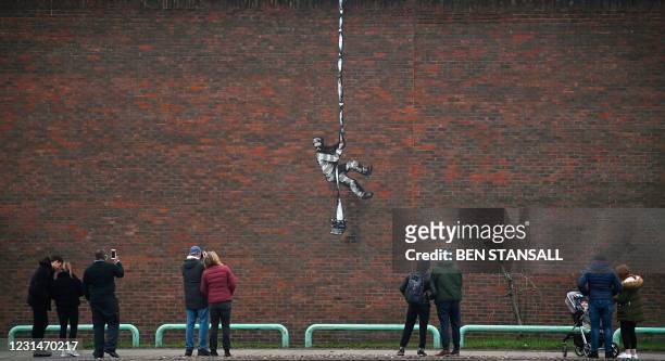 Members of the public pause to look at an artwork bearing the hallmarks of street artist Banksy on the side of Reading Prison in Reading, west of...