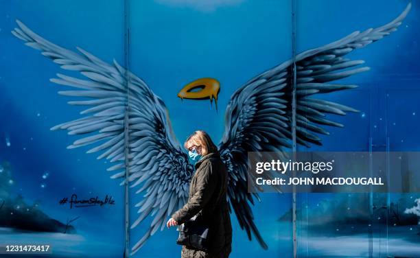 Woman wearing a face mask walks past a mural painting featuring an angel's wings and halo, at a shopping mall in south west Berlin on March 2 amid...