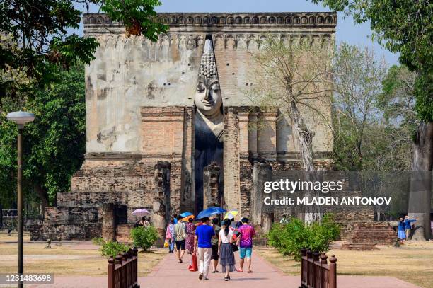This photograph taken on February 27, 2021 shows tourists visiting the giant Buddha statue at Wat Si Chum in the Sukhothai Historical Park, some...