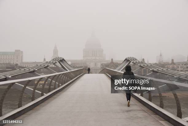 Woman walks along an empty Millennium Bridge on a murky day. Dense fog engulfed much of London today, as temperatures plummeted once again.