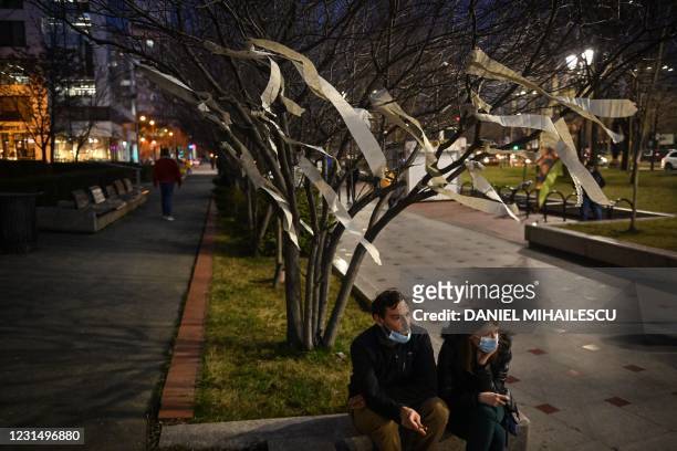 Couple is pictured next to a tree adorned by protesters with toilet paper strips during a protest in the front of Bucharest's Court March 3, 2021. -...