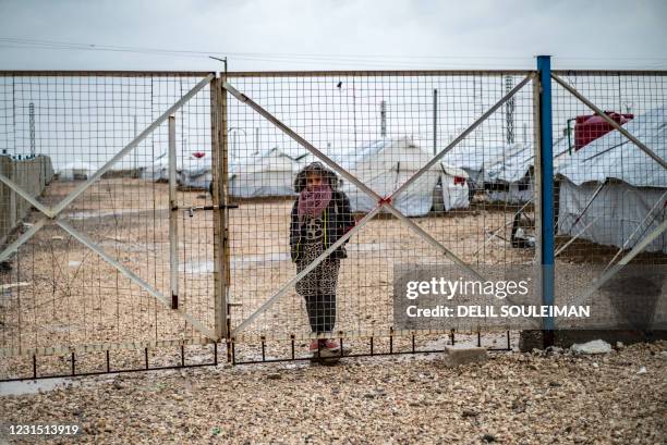 Youth looks out through a metal fence as she stands in the rain at Camp Roj, where relatives of people suspected of belonging to the Islamic State...