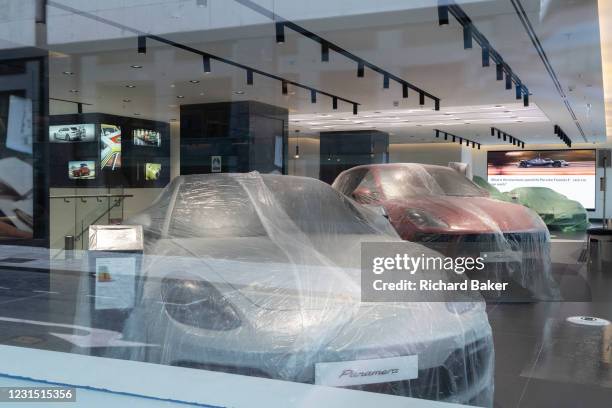 Protected against the dust during the closure of non-essential businesses during the Coronavirus pandemic, luxury Porsche cars are under cover in the...