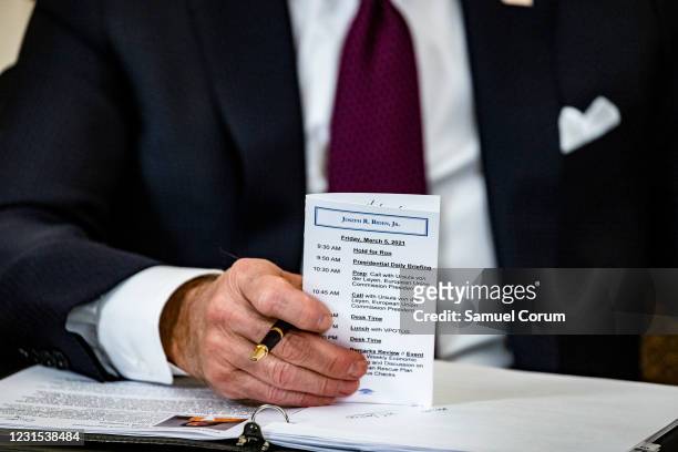 President Joe Biden reads the daily coronavirus numbers from a card that he says he always carries with him during a roundtable meeting with...
