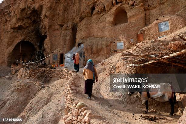 Hazara women walk along a path leading to the entrance of a cave where they live with their family at Tak Darakht village on the outskirts of Bamiyan...