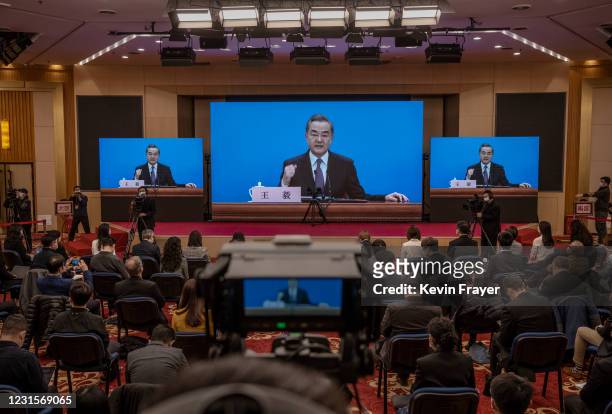 Chinese and foreign journalists watch as China's Foreign Minister Wang Yi, on screen, gestures as he answers a question during a video news...