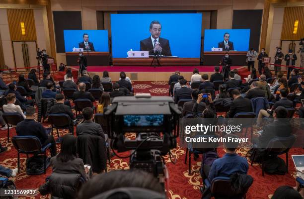 Chinese and foreign journalists watch as China's Foreign Minister Wang Yi, on screen, gestures as he answers a question during a video news...