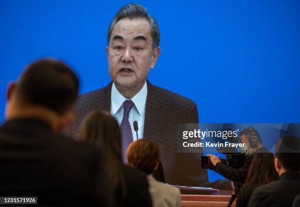 Chinese and foreign journalists watch as China's Foreign Minister Wang Yi, on screen, answers a question during a video news conference, held...