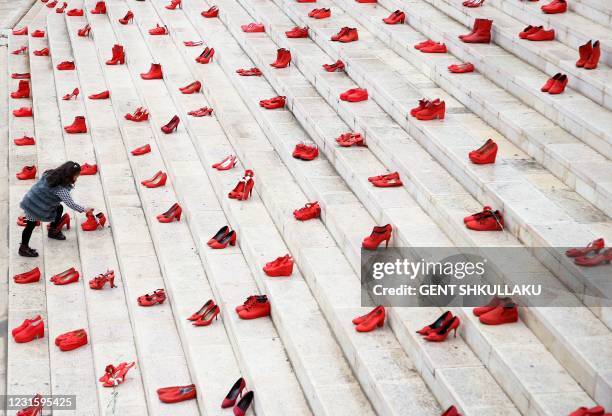 Girl puts flowers at an installation of women's red shoes displayed on staircase, as a symbol to denounce violence against women, at Durresi main...