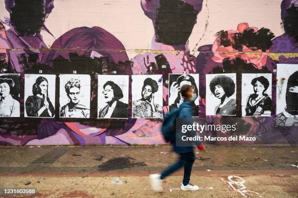 Young woman walks past by a feminist mural that appeared today vandalized during International Women's Day. Placards of women have been placed over...