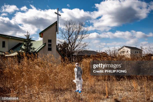 In this picture taken on February 27, 2021 reverend Akira Sato, wearing a protective suit, poses outside the old building of Fukushima First Bible...