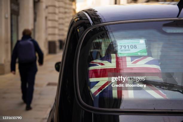 Cushion with the design of a British Union flag, also known as a Union Jack, in the back window of a traditional black taxi in the City of London,...