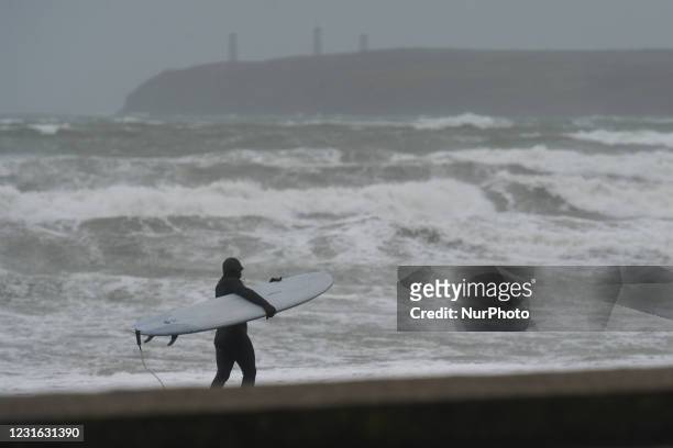 Surfer on the beach at Tramore in County Waterford on the South East coast of Ireland, where the yellow 100 km/h weather warning is in effect. On...