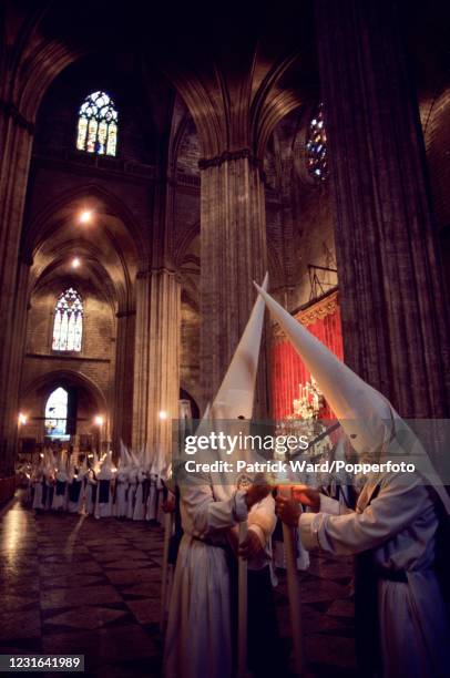 Cofradias, members of a religious brotherhood, wearing long white robes and capriotes or conical hats lighting tall candles in the Cathedral during...