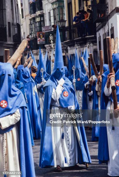 Hooded cofradias or brotherhoods, wearing long blue robes and capirotes or conical hats, some carrying crosses, parading through the streets during...