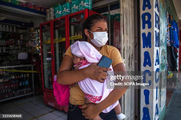 Woman wearing a face mask while carrying her daughter stands at the entrance of the pharmacy. In Mexico, the second economic power in Latin America,...