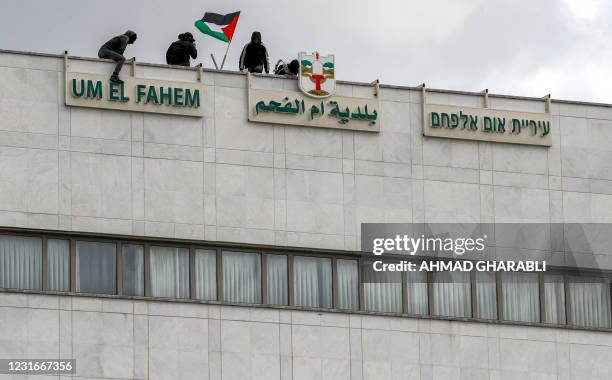 Demonstrators with a Palestinian flag stand atop the roof of the local municipality building of the mostly Arab city of Umm al-Fahm in northern...
