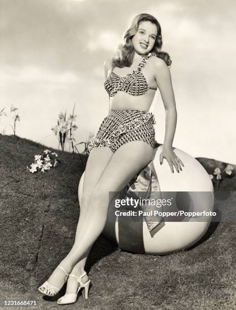Studio portrait of Diana Dors, English film and television actress, wearing a two-piece bathing costume and sitting on a large Easter egg, circa 1950.