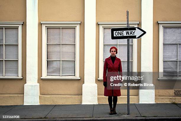 woman standing on street under one way sign - one way communication stock pictures, royalty-free photos & images