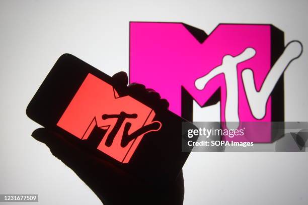 In this photo illustration a silhouette hand is seen holding a smartphone with MTV channel logo on a its screen.