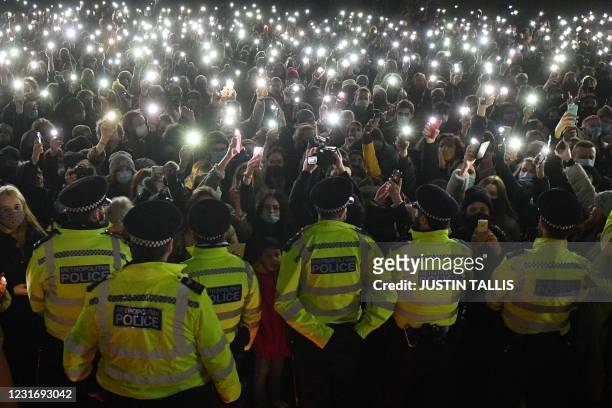 Police officers form a cordon as well-wishers turn on their phone torches as they gather at a band-stand where a planned vigil in honour of alleged...