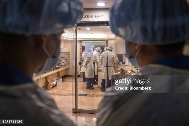Government workers wearing personal protective equipment stand in the lobby of a residential building in an area under lockdown on Pok Fu Lam Road in...