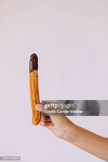 hand holding a single chocolate dipped churro in front of a white background - churro stockfoto's en -beelden