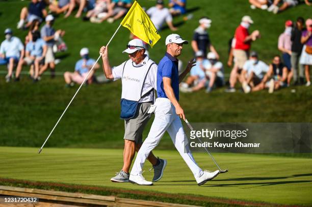 Justin Thomas waves his ball to fans after making a birdie putt on the 16th hole green as his caddie Jimmy Johnson puts the pin back during the final...