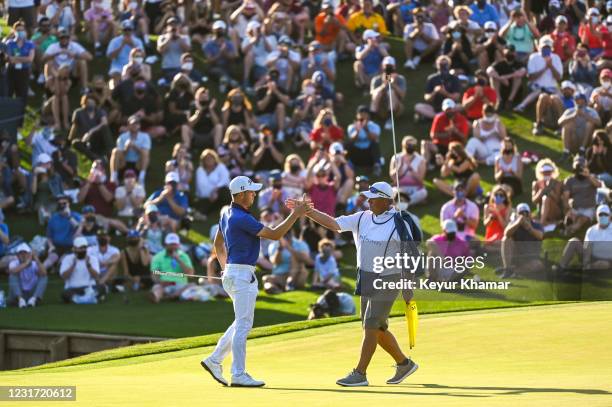 Justin Thomas celebrates with his caddie Jimmy Johnson after making his par putt on the 18th hole green as fans applaud during the final round of THE...