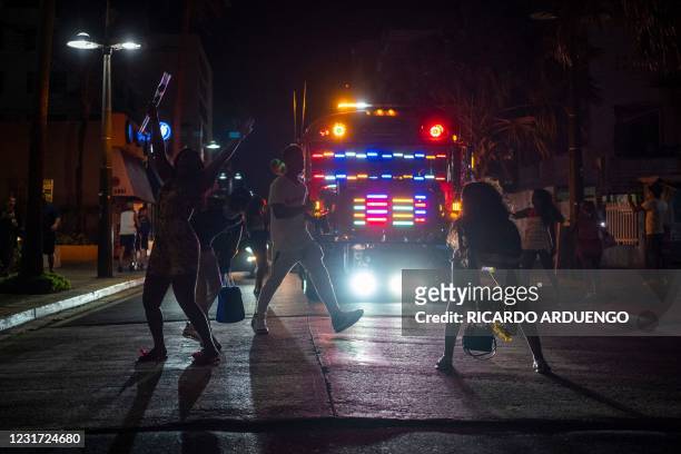 Tourists dance on the middle of the street in front of a party bus in the tourist zone of El Condado in San Juan, Puerto Rico on March 14, 2021.
