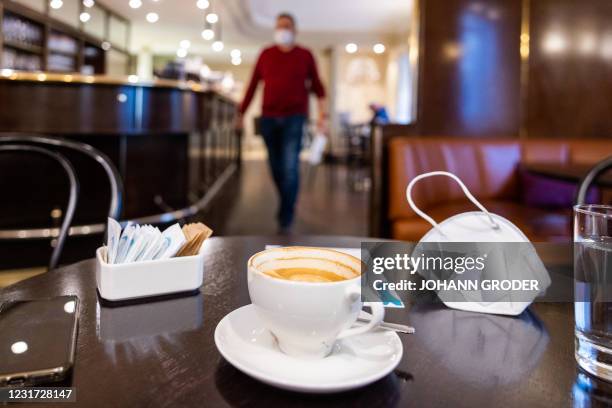 Photo taken on March 15, 2021 shows a face mask placed on a table next to cup of coffee at a cafe in Bludenz, in the western Austrian state of...