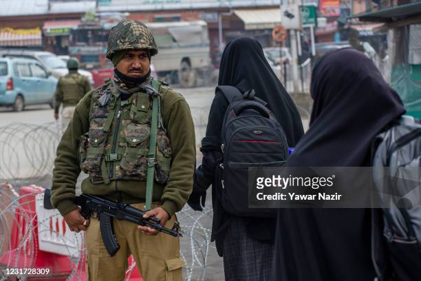Kashmiri Muslim women walk past Indian paramilitary soldier guarding his bunkers on a main road, on March 15, 2021 in Srinagar, the summer capital of...